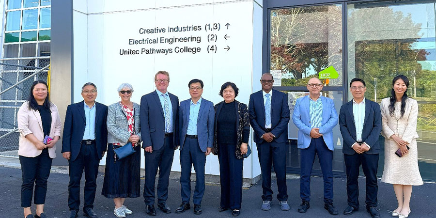 Staff from Shanghai Polytechnic University, MIT and Unitec smile outside a building on the Mt Albert campus.