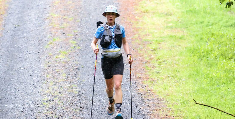 Kate Lewis power-walking outdoors with walking sticks.