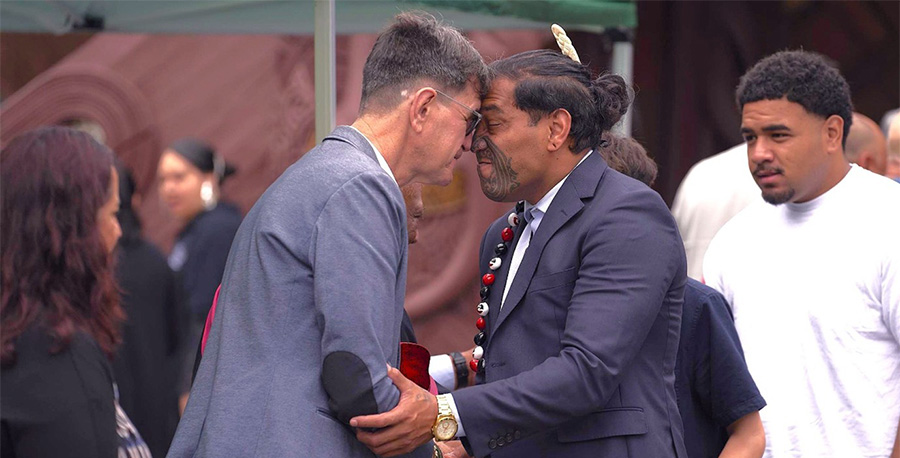 Two men in suits share 'hongi' during a pōwhiri.