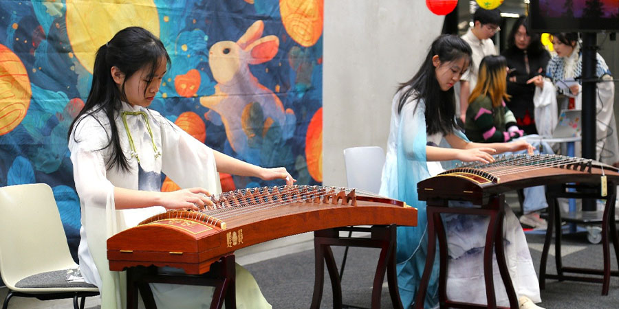 Two women in traditional Chinese attire each play a guzheng.