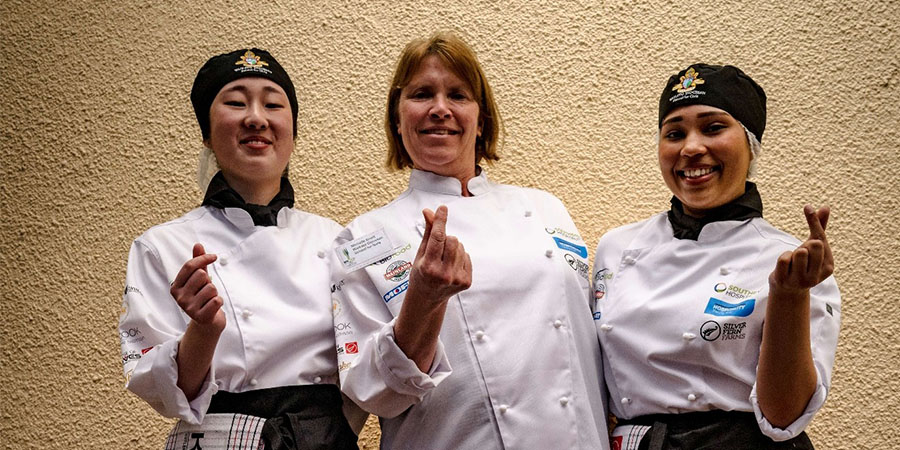 Two students and their teacher smile for the camera.