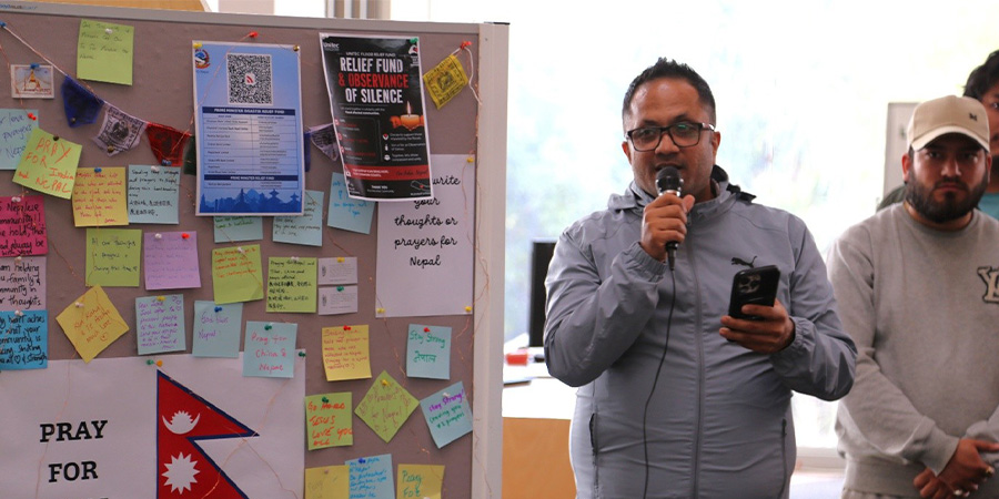 Everest Nepalese Student Club president Nilam Adhikari gives a speech next to a noticeboard with prayers for Nepal.
