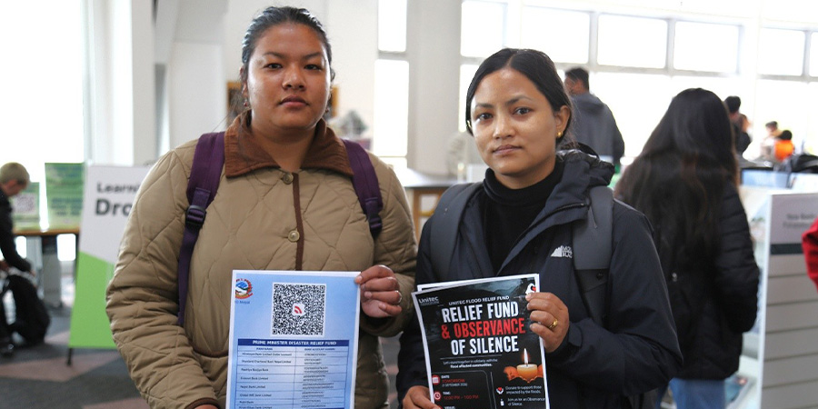 Two students pose with posters about the Nepal flood relief appeal.