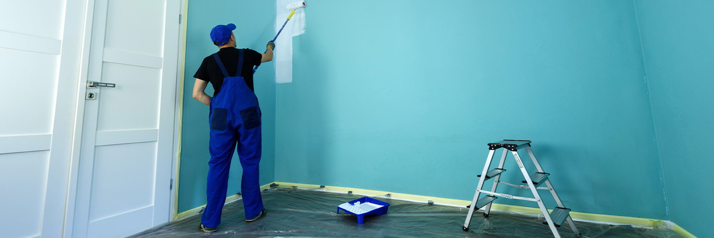 A person in work overalls paints a wall.