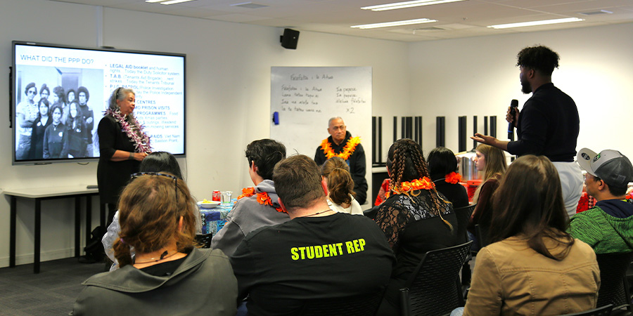 A young man stands to ask a question of the two speakers in a class full of people.