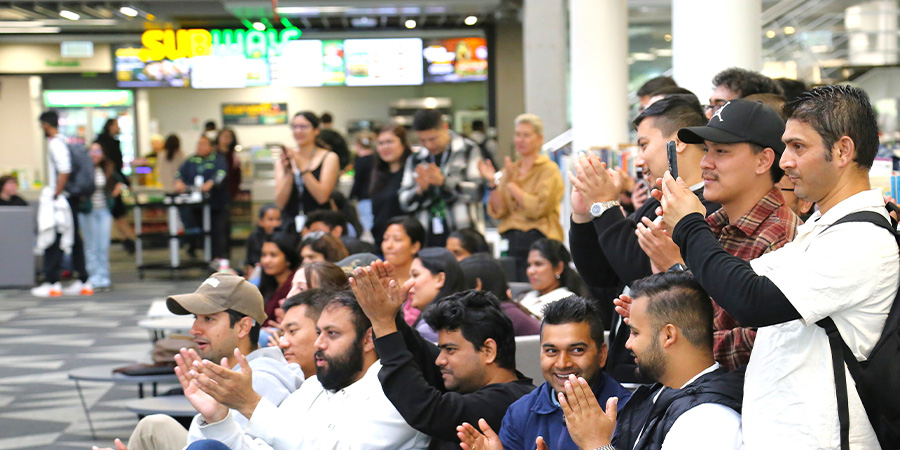 A large group of students watch a performance in a light-filled indoor space.