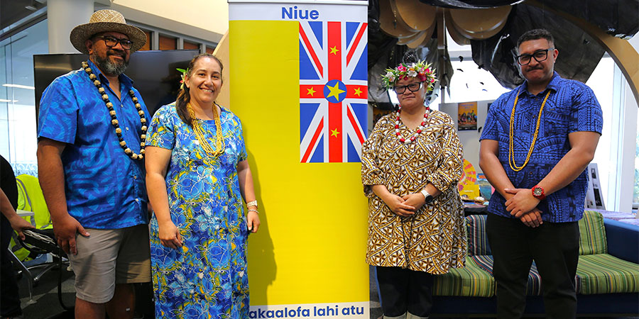 Four people in traditional Pacific attire smile for the camera.