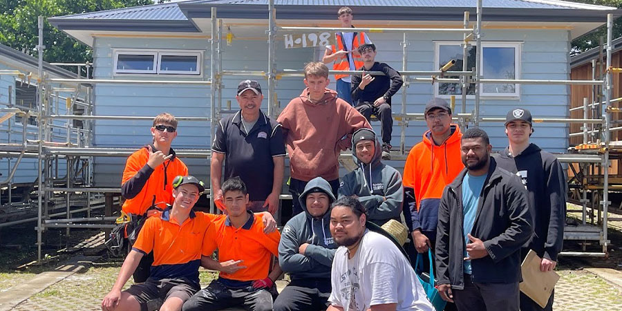 A group of Carpentry students smile for the camera in front of one of the houses they built.