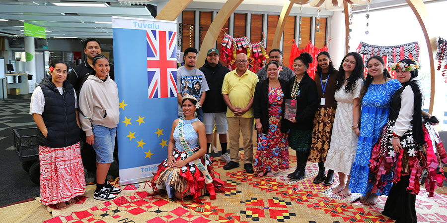 A group of staff smile for the camera in front of the flag of Tuvalu.