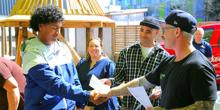 A man hands a certificate to a young man in a hoodie while two other people look on.