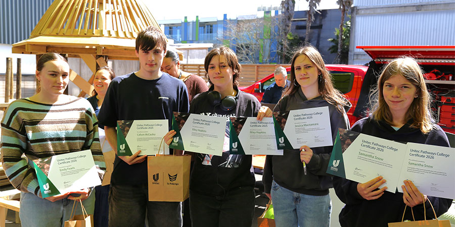 Four young people hold up certificates and smile.